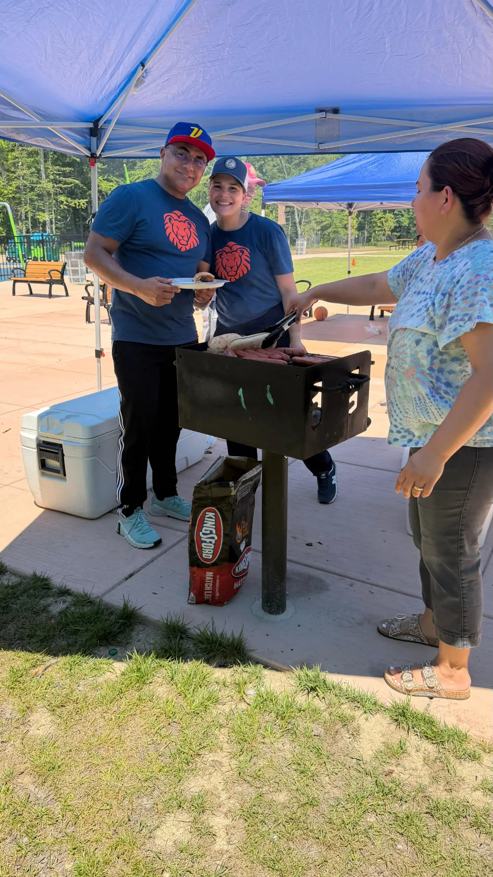Adults serving at a community gathering under a canopy.