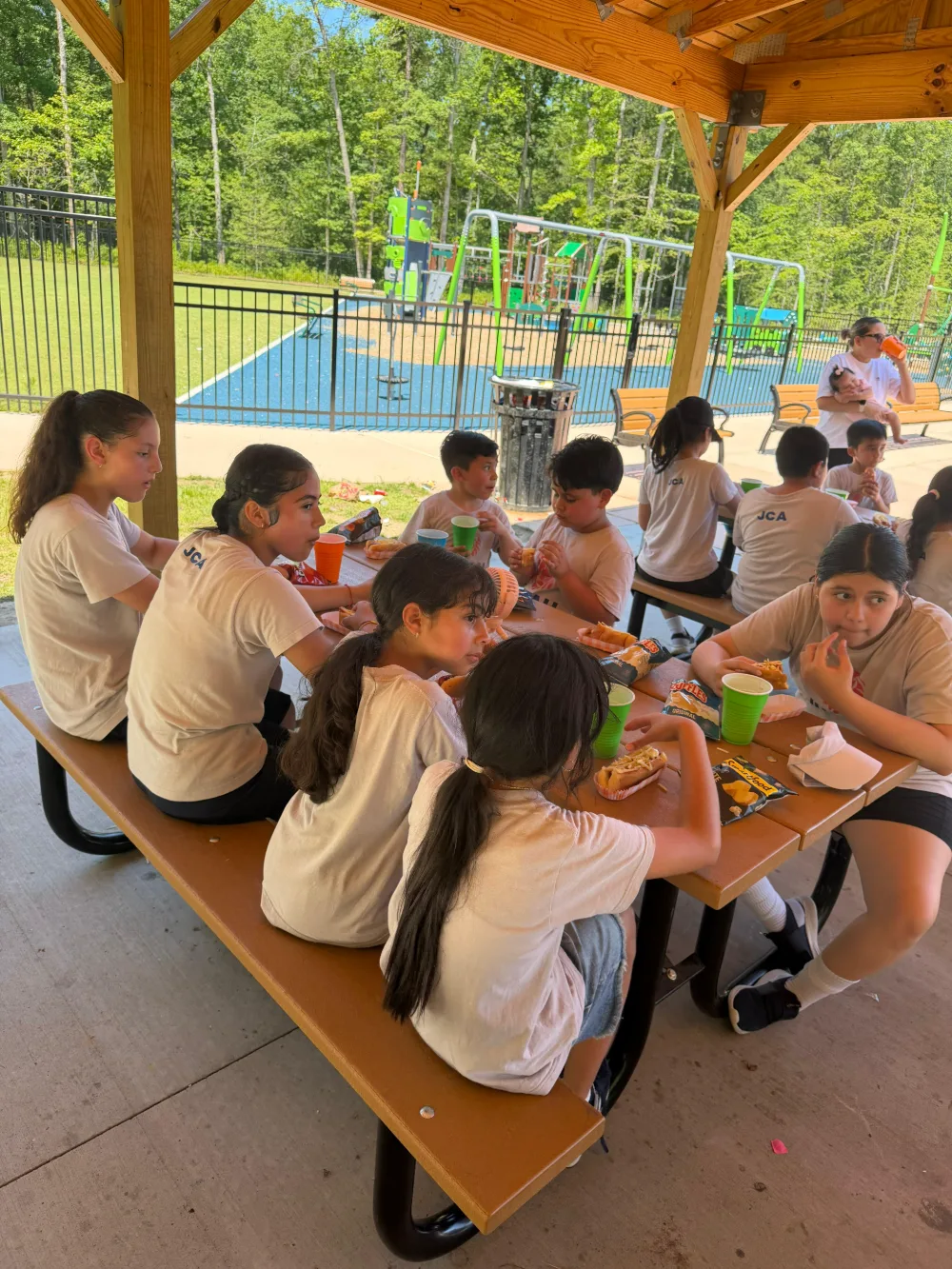 Families and students together under an outdoor pavilion at a community gathering.