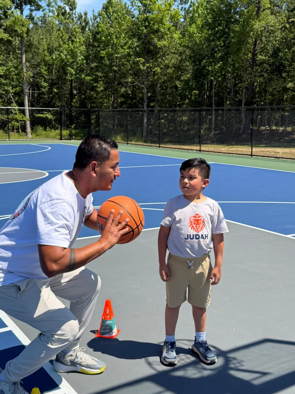 An adult and a student with a basketball on the outdoor court.